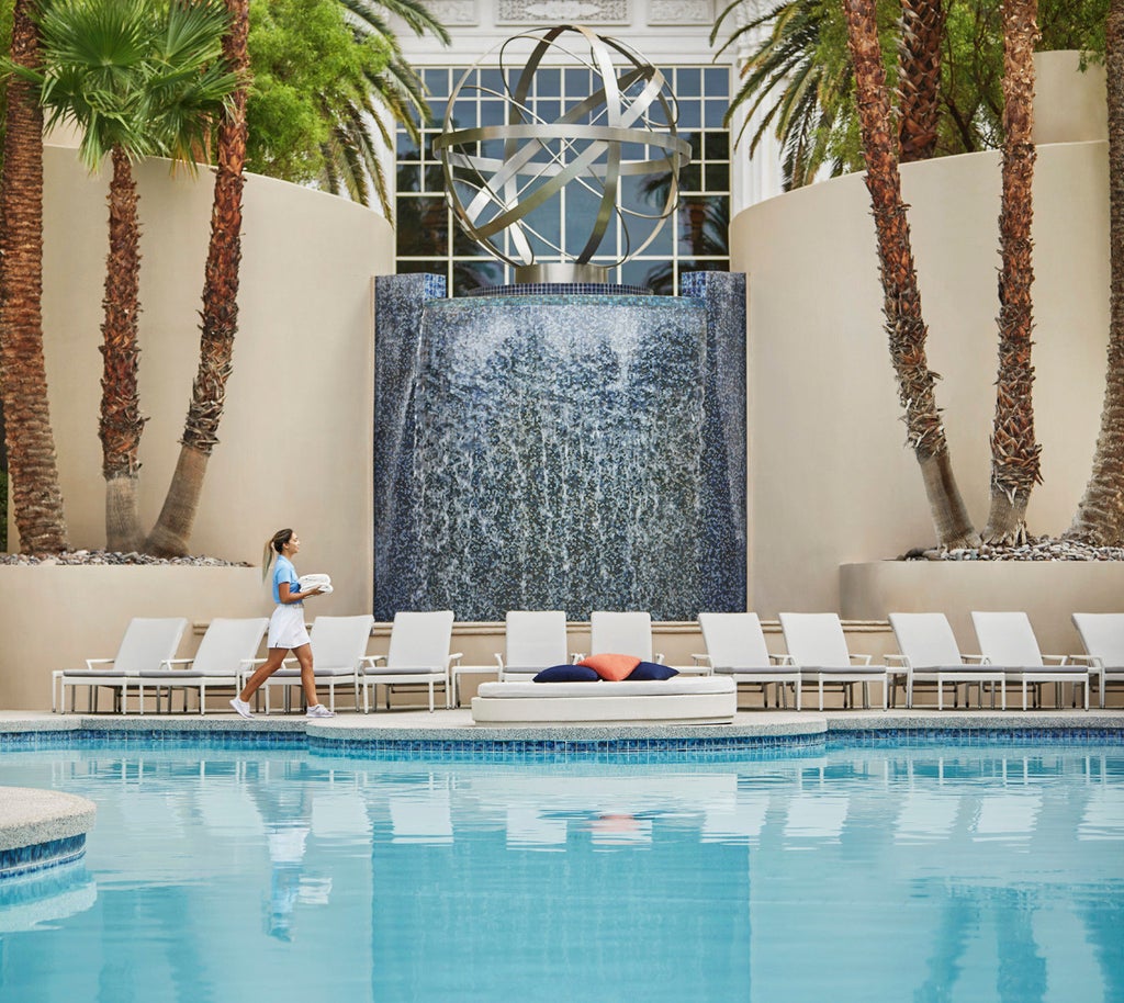 Luxurious Four Seasons Las Vegas exterior with golden-lit facade, palm trees, fountain plaza, and dramatic desert sunset backdrop