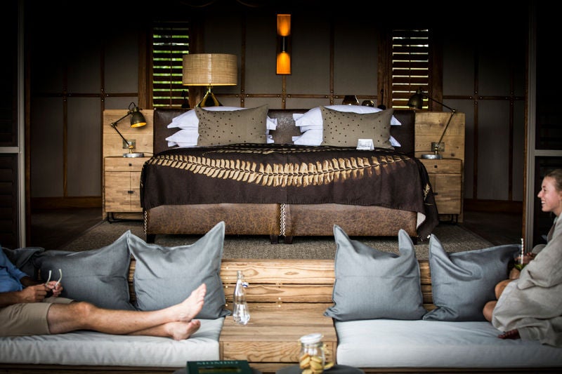 Elevated luxury safari tent perched on wooden deck overlooking vast Okavango Delta, surrounded by acacia trees and golden grasslands