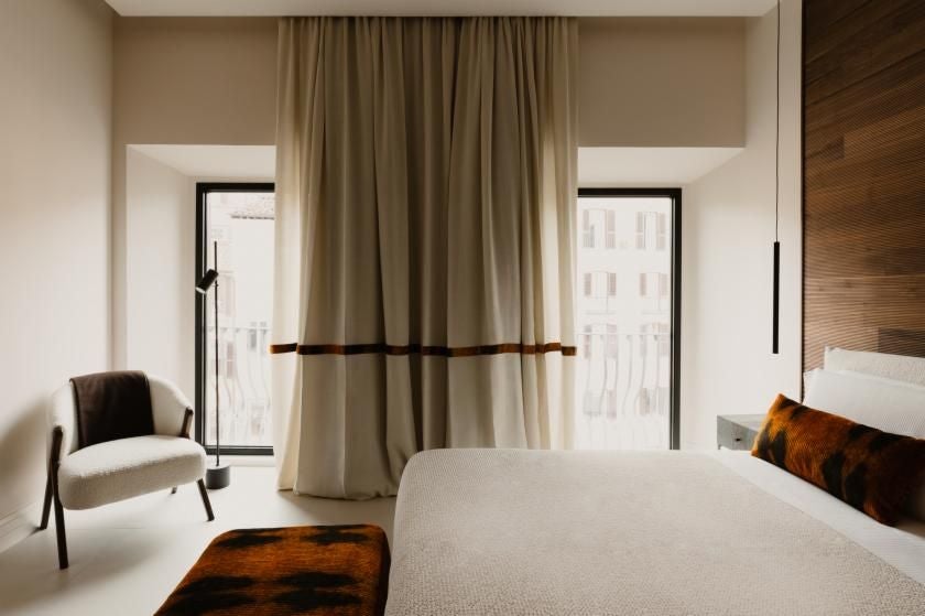 Elegant Rome hotel room with plush white bedding, vintage chandelier, soft neutral tones, ornate window overlooking historic Piazza di Spagna neighborhood