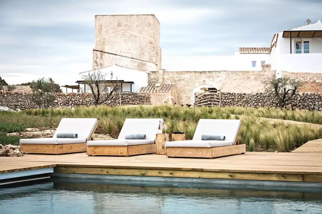 Elegant stone tower hotel overlooking Mediterranean coastline, golden sunlight illuminating rustic stone walls and lush surrounding landscape