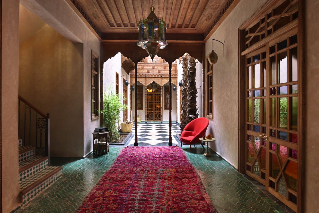 A luxurious Moroccan courtyard with emerald-green pool, pink walls, ornate archways, lush plants and traditional lanterns at El Fenn hotel