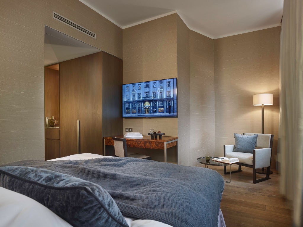 Elegant queen-size bed with rich wooden furnishings, soft neutral tones, and large windows overlooking a charming Prague courtyard in a luxurious boutique hotel room