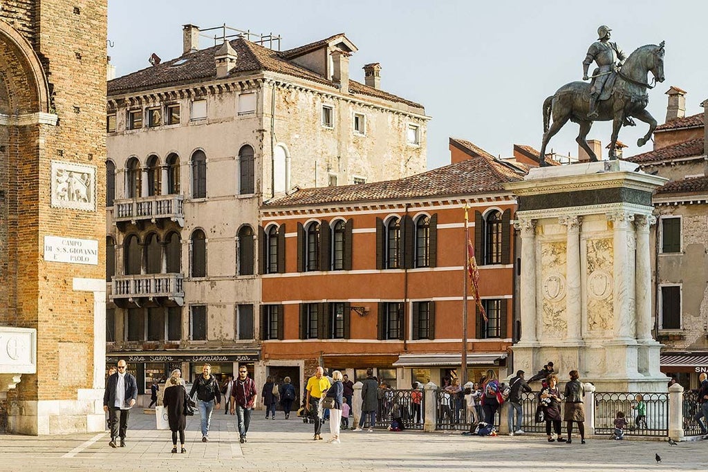 Elegant Renaissance-style palazzo with ornate balconies overlooking Venice's Grand Canal, golden sunlight illuminating historic stone facade and architectural details