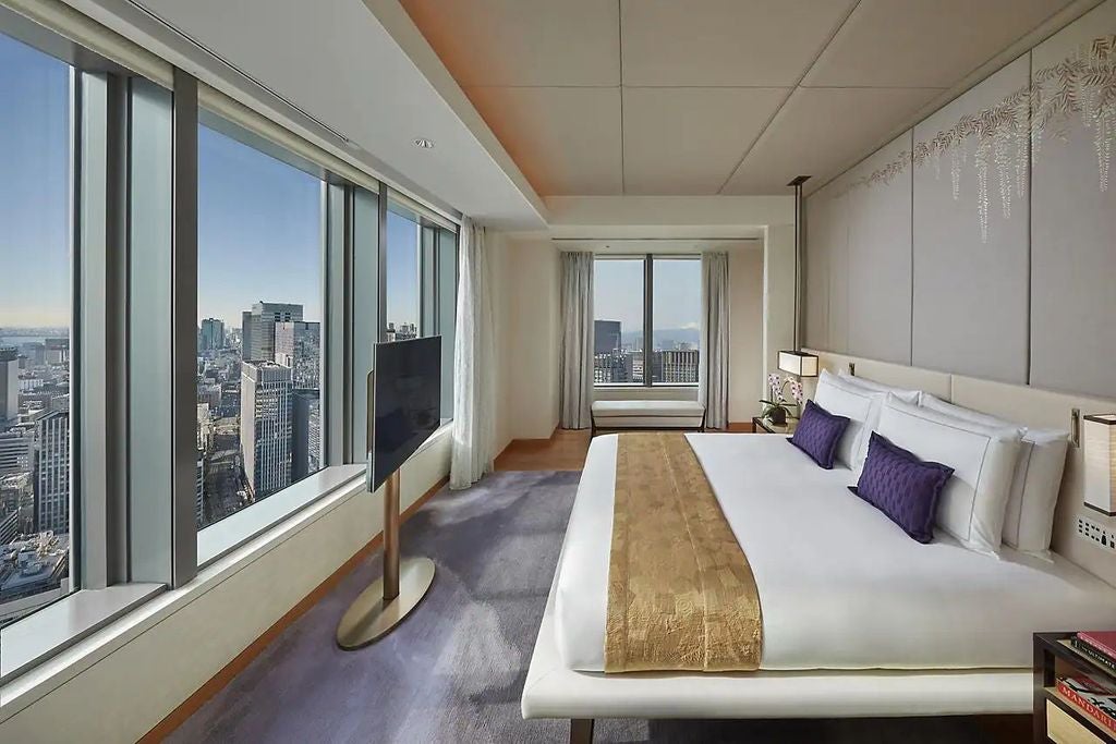 Luxurious suite with floor-to-ceiling windows overlooking Tokyo skyline, featuring modern Asian decor, plush king bed and marble bathroom