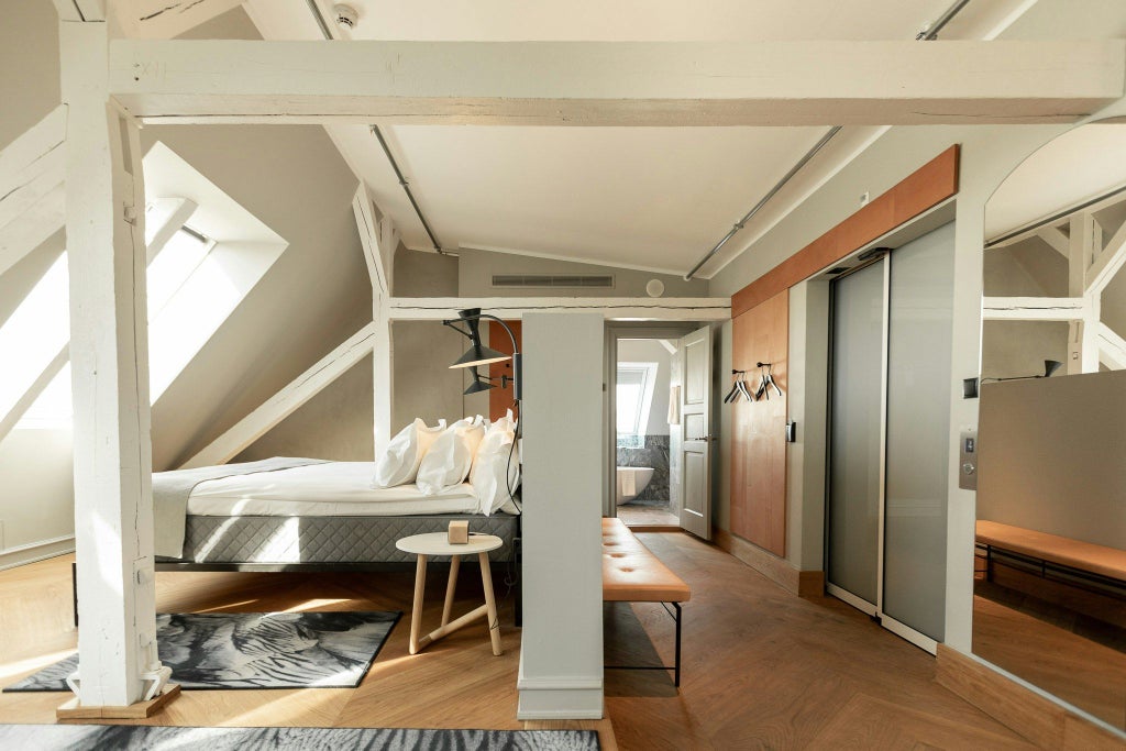 Luxurious penthouse suite with minimalist Nordic design, panoramic city views, elegant king bed, and sleek contemporary furnishings in Copenhagen.