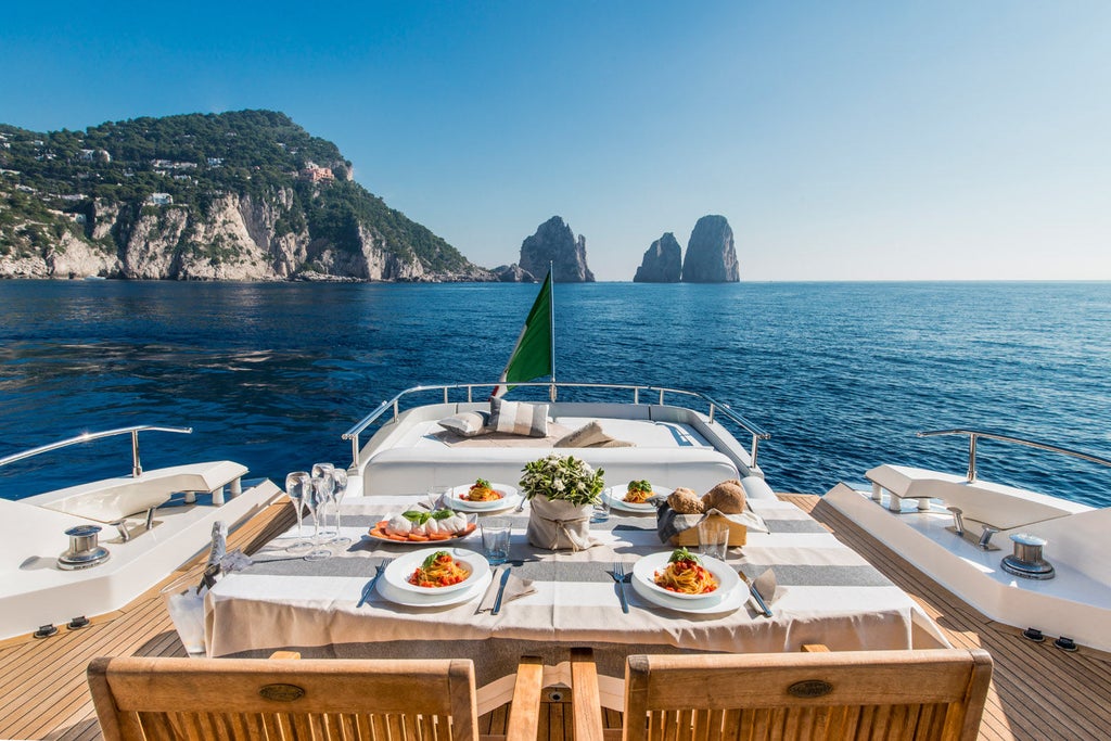 Elegant Italian yacht hotel with white and teak exterior docked in crystal-clear Mediterranean waters against mountainous coastline backdrop