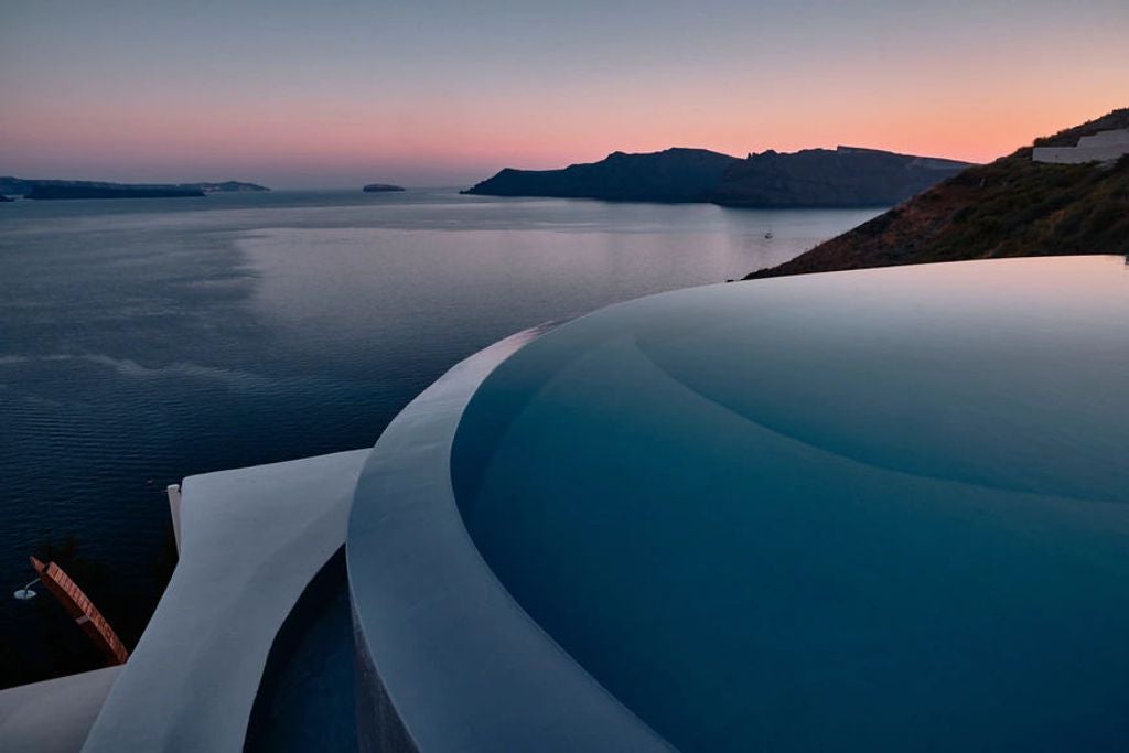 Luxurious infinity pool overlooking Santorini's caldera at sunset, with white curved architecture and Mediterranean Sea views