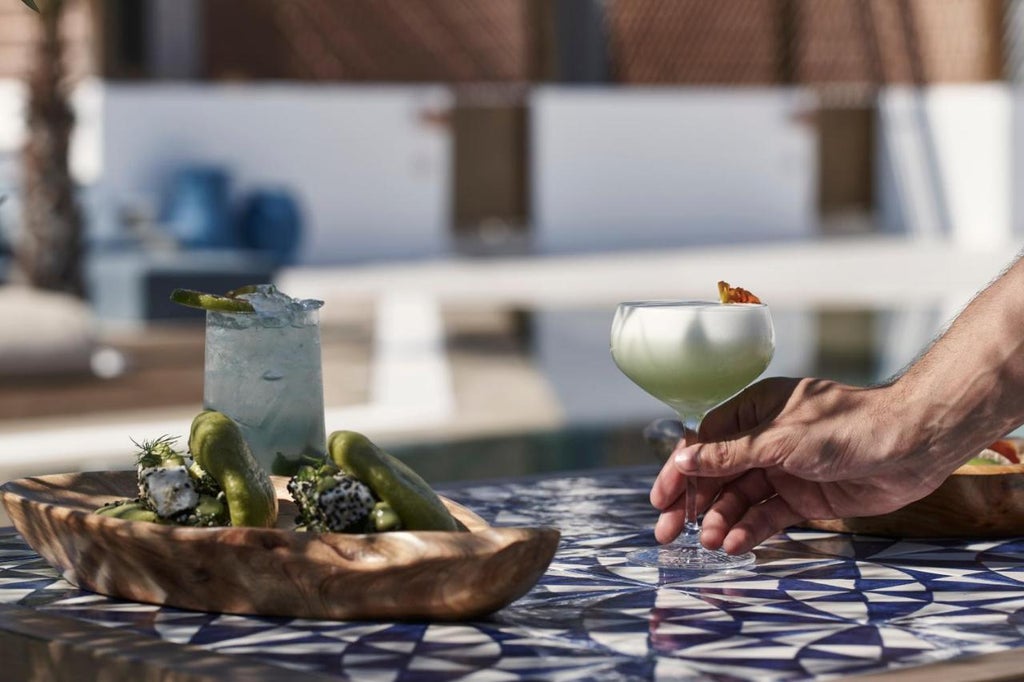 Elegant white-walled Greek hotel with infinity pool overlooking Aegean Sea, modern sun loungers and umbrellas against mountain backdrop