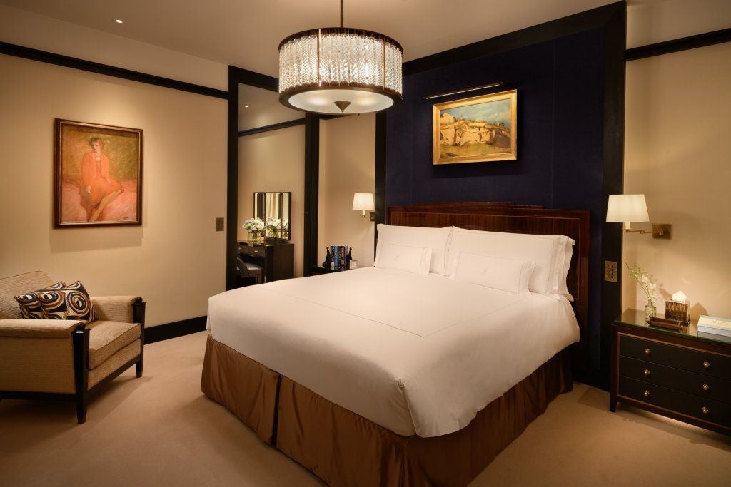 Elegant Mayfair suite with plush king bed, luxurious cream and gold color palette, modern art deco furnishings, and expansive city view windows