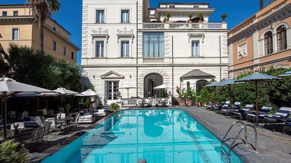 Elegant 5-star luxury hotel exterior with neoclassical architecture, white marble facade, and manicured gardens overlooking a scenic Italian cityscape at sunset