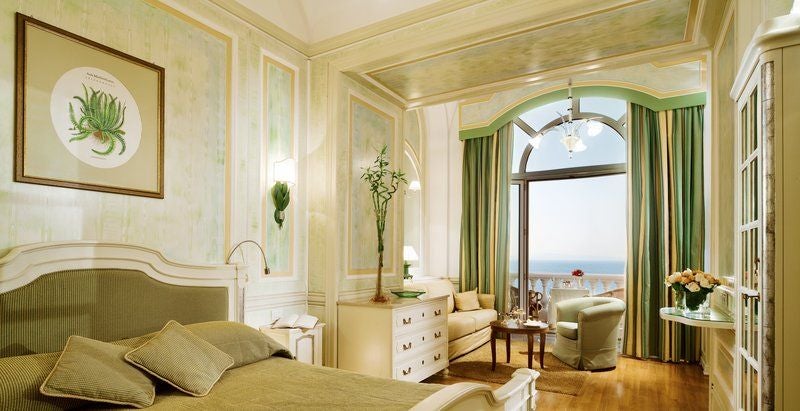 Elegant balcony room with ornate period furniture, crystal chandelier and panoramic Mediterranean Sea views through French doors