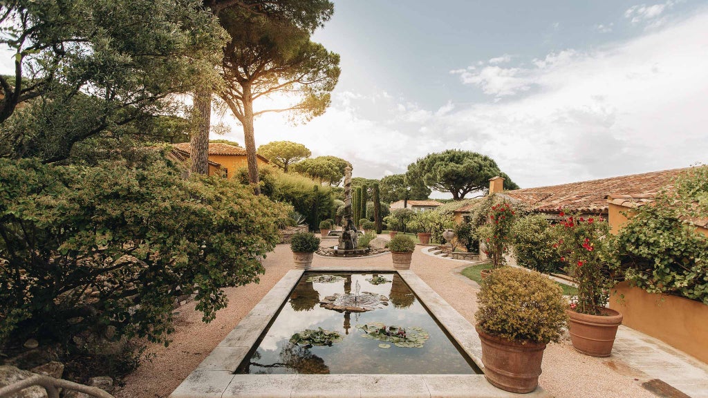 Luxurious Mediterranean villa nestled in Saint-Tropez, with elegant white façade, lush green gardens, and azure swimming pool amid vibrant French Riviera landscape