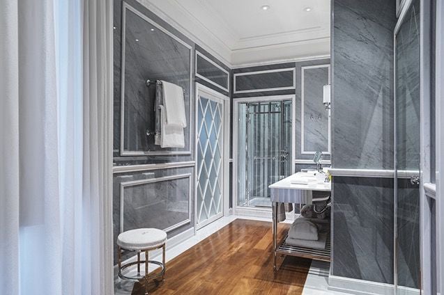 Elegant Italian hotel room with marble bathroom, plush white bedding, gold accents, and panoramic window overlooking Roman architectural landscape