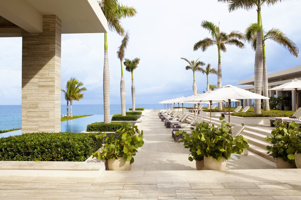 Modern beachfront resort with infinity pools overlooking turquoise Caribbean waters, white sand beach, and luxury cabanas at sunset.