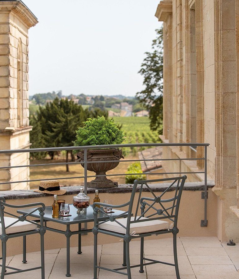 Elegant terrace room with plush white bedding, designer furniture, and expansive French vineyard views at La Maison d'Estournel luxury accommodation