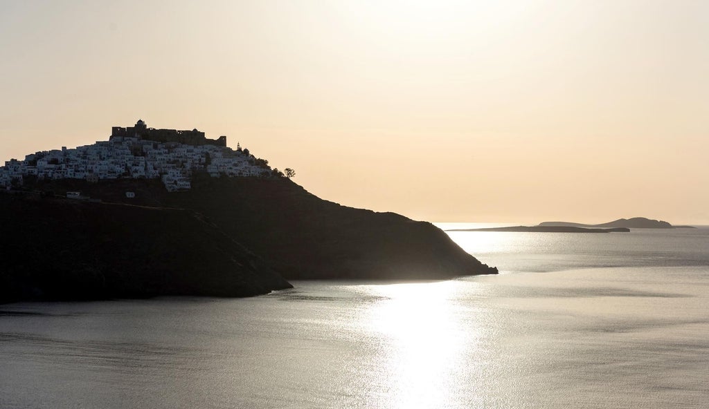 Elegant whitewashed suites with blue-domed roofs overlooking azure Aegean waters, nestled in the picturesque landscape of a Greek island destination