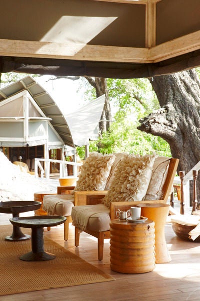 Safari-style luxury tent elevated on wooden platforms overlooking vast Okavango Delta wetlands at sunset, featuring private plunge pool