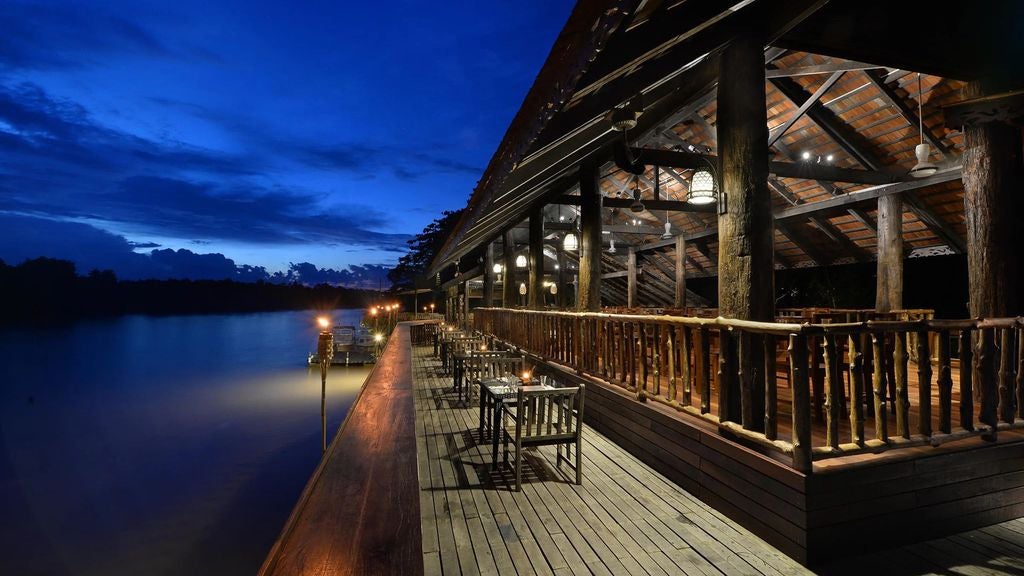 Elevated wooden lodge with modern architecture nestled in dense rainforest, featuring river-view terraces and plush outdoor seating