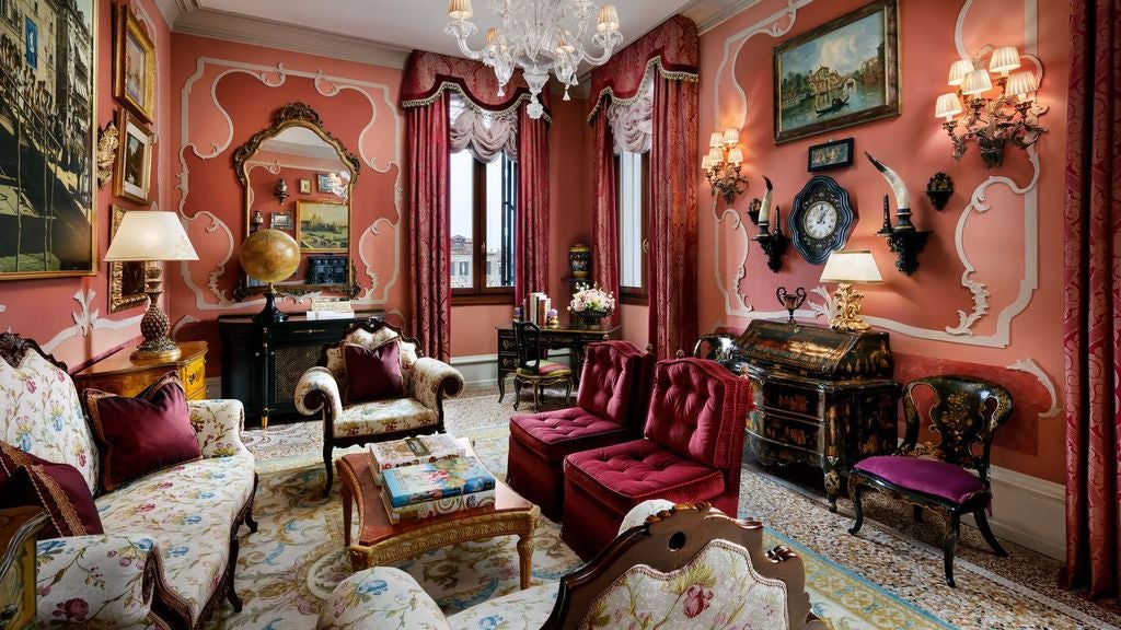 Opulent Venetian suite with ornate gold-framed mirrors, crystal chandelier, antique furnishings, and plush striped sofa overlooking canal views