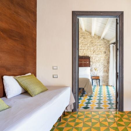 Elegant rustic Italian hotel room with stone walls, wooden furnishings, minimalist design, warm terracotta tones, and soft natural light streaming through arched window