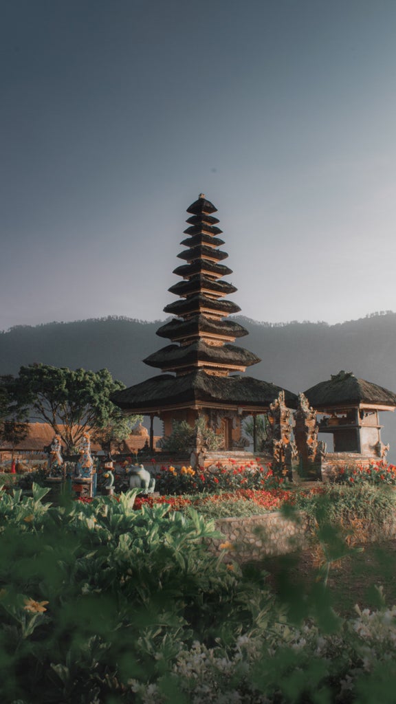 Traditional wooden Balinese gateway with ornate stone carvings and lush tropical foliage leads to a luxury beachfront resort at sunset