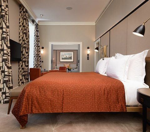 Elegant hotel room with floor-to-ceiling windows overlooking the Tagus River, featuring a king bed with crisp white linens and chic decor