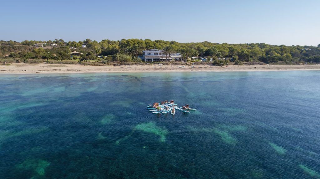 Sleek white beachfront hotel with minimalist design, turquoise infinity pool overlooking Mediterranean coastline at golden sunset in Spain