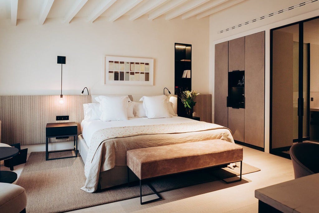 Elegant boutique hotel room with plush white bedding, marble-like surfaces, modern minimalist decor, and soft natural lighting in Spain