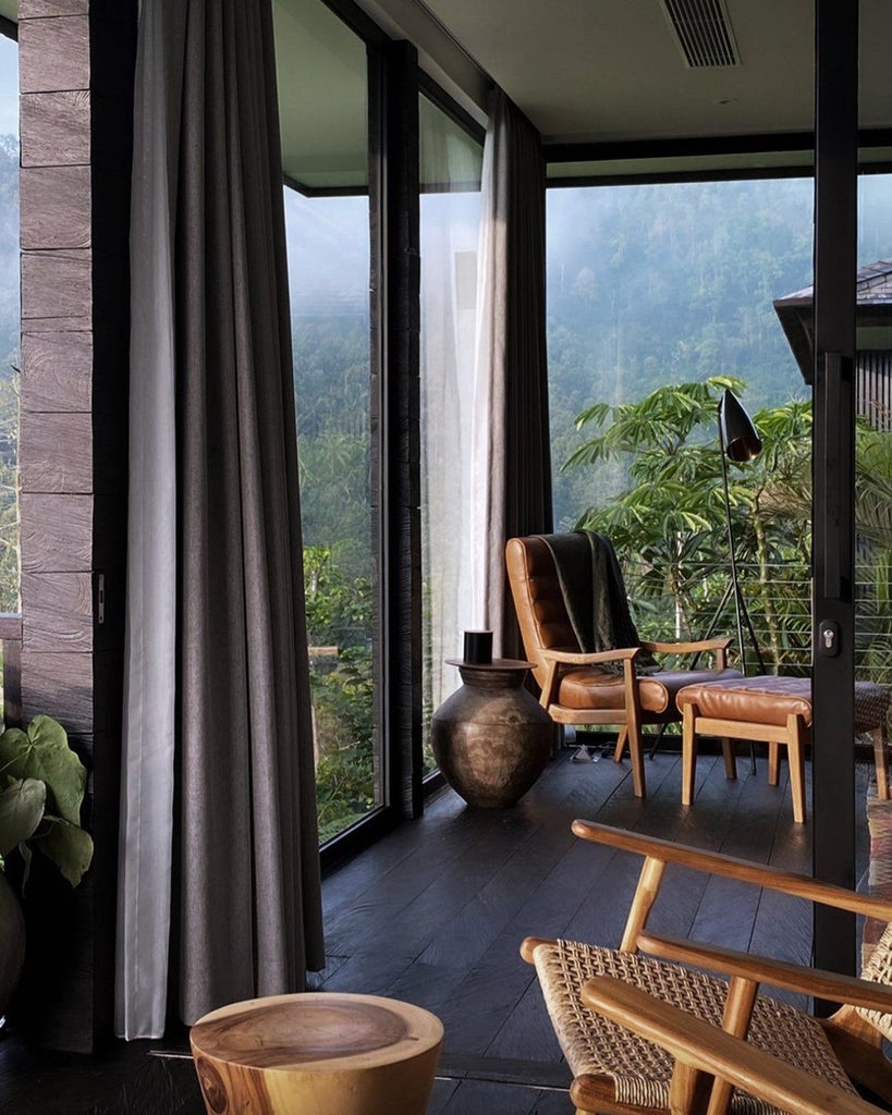 Luxury treehouse-style wooden cabin with floor-to-ceiling windows perched on stilts amid lush Balinese jungle, mountain views at sunset