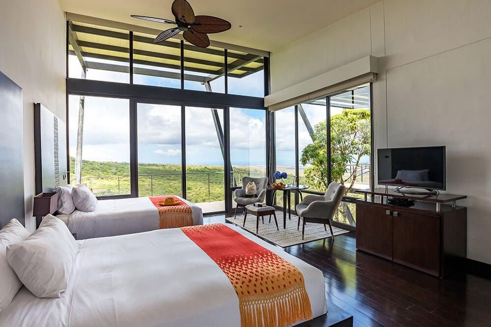 Luxurious balcony room at Pikaia Lodge with panoramic Galápagos volcanic landscape, modern design, and expansive ocean view through glass doors