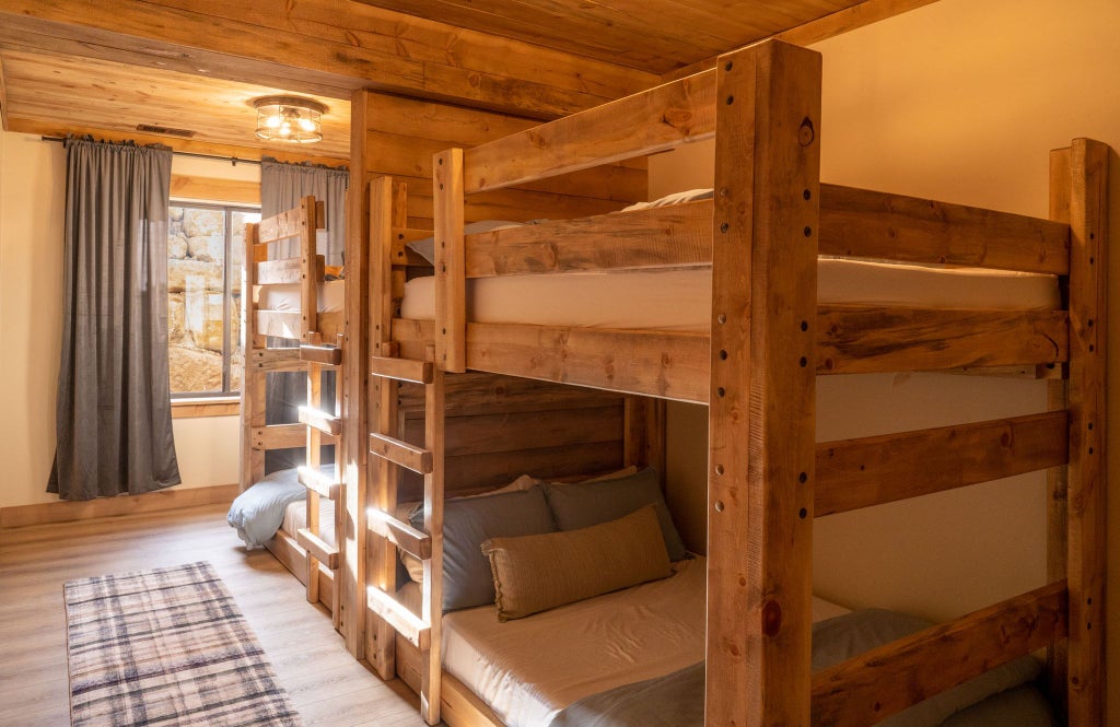 Rustic wooden lodge bedroom with plush bedding, stunning mountain landscape view, warm ambient lighting, and elegant wilderness-inspired decor in scenic United States retreat