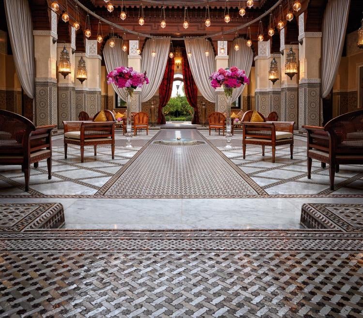 Elegant Moroccan hotel façade with ornate Islamic architecture, grand arched windows, and palm trees lining a pristine courtyard entrance