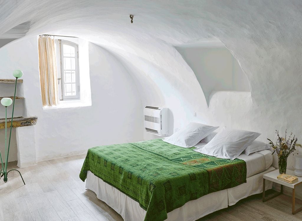 Elegant stone-walled bedroom with antique wooden furnishings, soft linens, and warm natural light streaming through rustic French windows in Provence