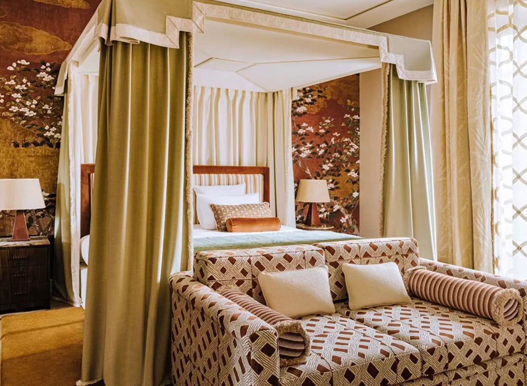 Opulent Parisian hotel room with black and gold leopard print wallpaper, crystal chandelier, and vintage-style furniture overlooking garden views