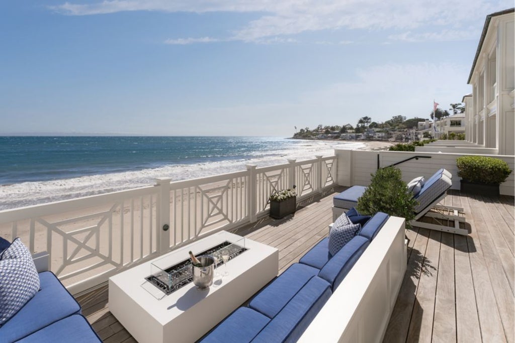 Luxurious beach house suite at Scenset Miramar with ocean-inspired decor, crisp white linens, and panoramic coastal view through floor-to-ceiling windows