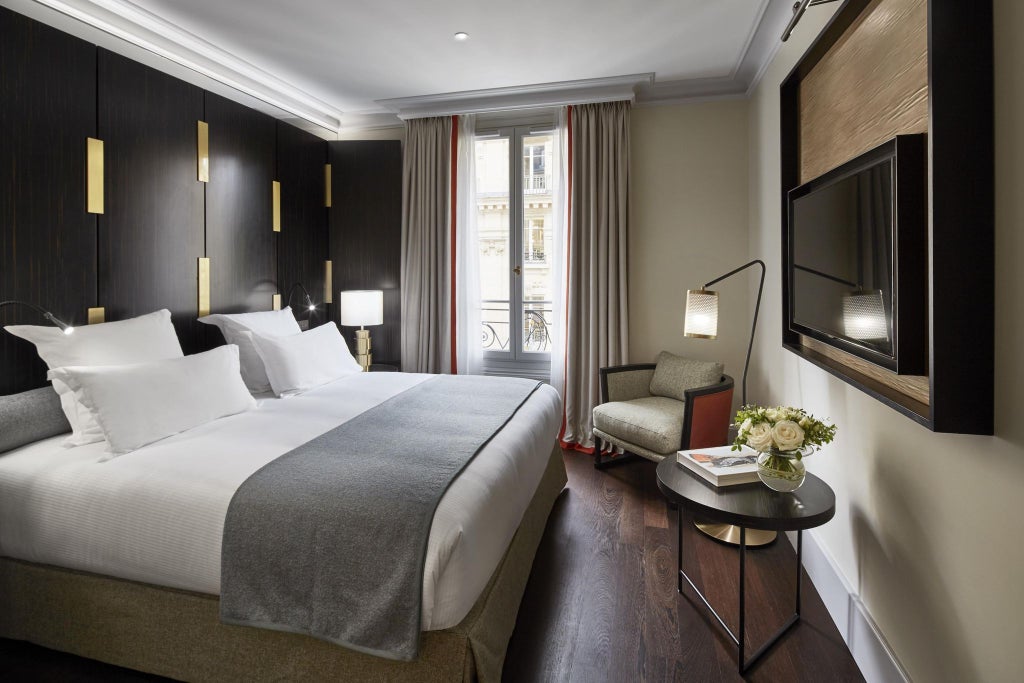 Elegant Parisian hotel room with plush bedding, rich wood furnishings, soft neutral tones, and large windows offering sophisticated urban luxury