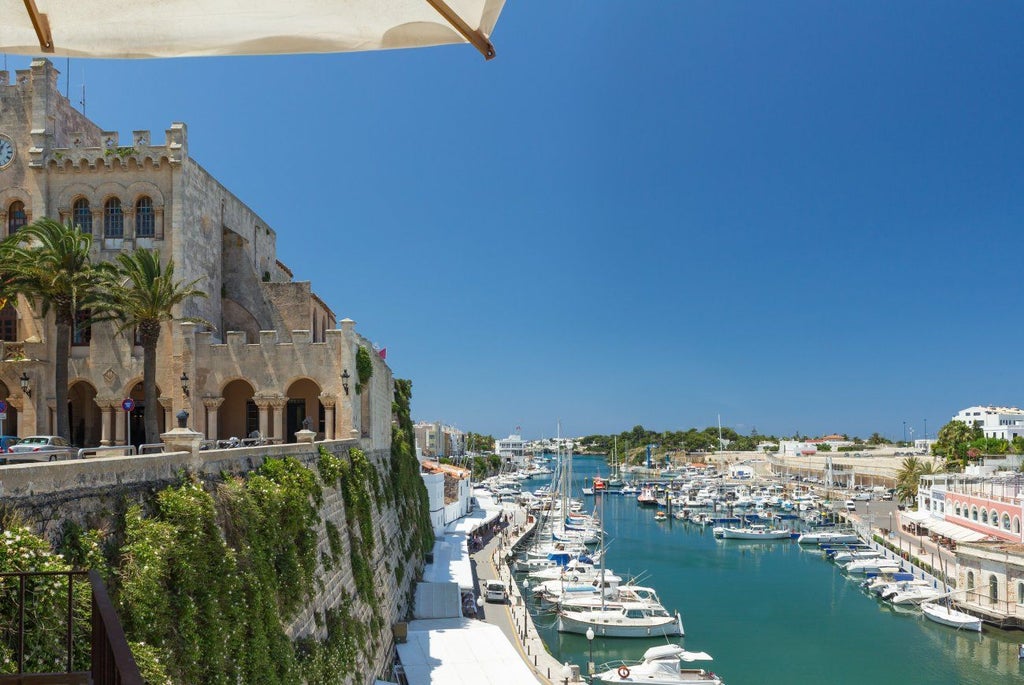 Luxury beachfront hotel with white Mediterranean architecture, azure pool, palm trees, and panoramic sea view in scenic Menorca, Spain