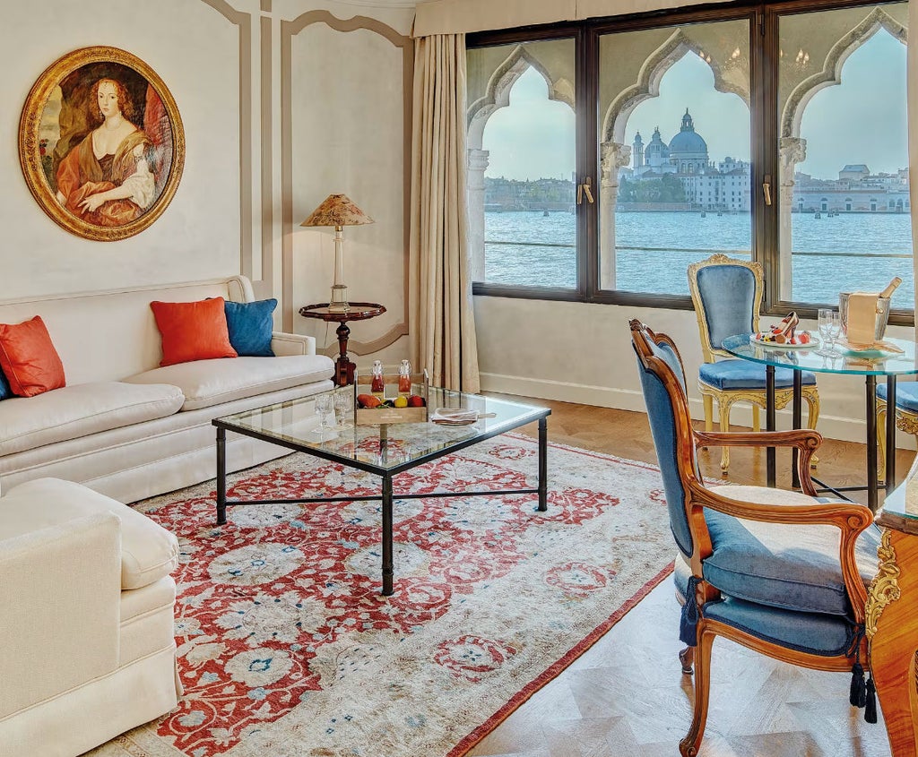 Opulent suite with floor-to-ceiling windows overlooking Venice's St. Mark's Basin, featuring antique furniture and pastel-toned décor