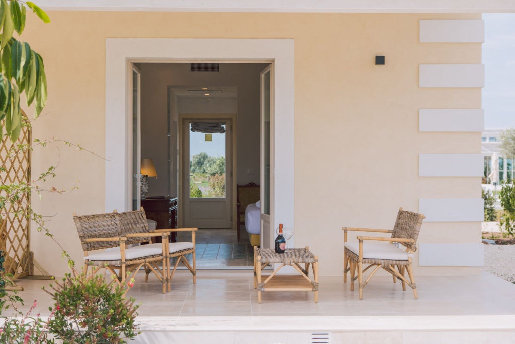 Elegant Italian boutique hotel room with refined decor, soft neutral tones, luxurious white linens, and traditional Sicilian architectural details at sunset