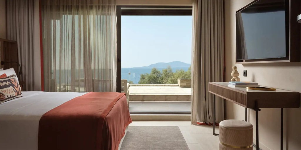 Elegant sea-facing junior suite with panoramic Aegean views, featuring plush white bedding, modern minimalist design, and expansive private balcony overlooking blue waters.