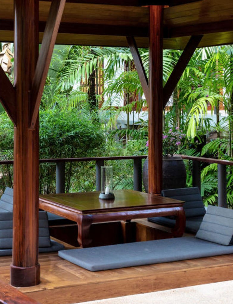 Contemporary Thai luxury pavilion with teak floors, sloped ceiling, king bed, and private terrace overlooking lush tropical gardens