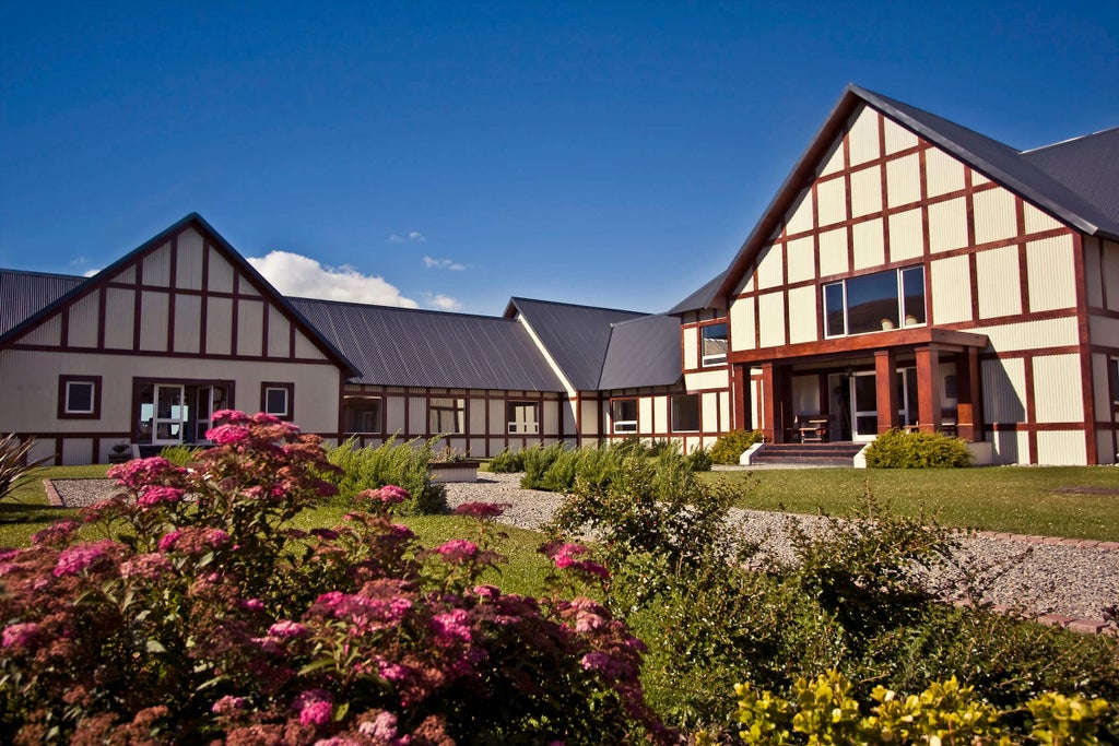 Modern luxury lodge with floor-to-ceiling windows overlooking Patagonian plains, snow-capped mountains, and Lake Argentino under blue skies