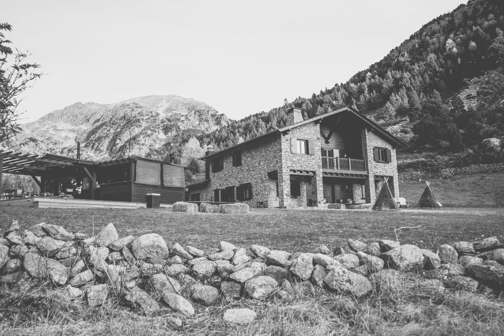 Luxurious mountain lodge nestled in Andorran peaks, featuring rustic stone exterior, expansive windows, and snow-capped mountain backdrop with elegant alpine architecture