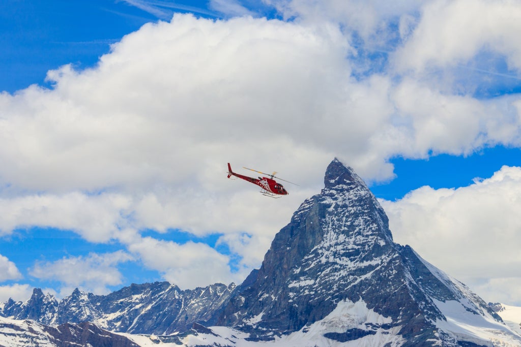 Sleek black helicopter hovering above snow-capped Swiss Alps near Zermatt, with majestic Matterhorn peak in dramatic background during golden alpine sunrise