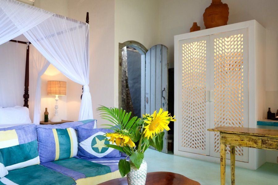 Rustic wooden bed with white linens in a minimalist Brazilian luxury hotel room with terracotta tiles and natural light streaming through large windows