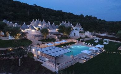 Luxurious stone trulli houses at Scenset Hotel, nestled in Puglia's countryside with rustic white walls and traditional conical roofs at sunset