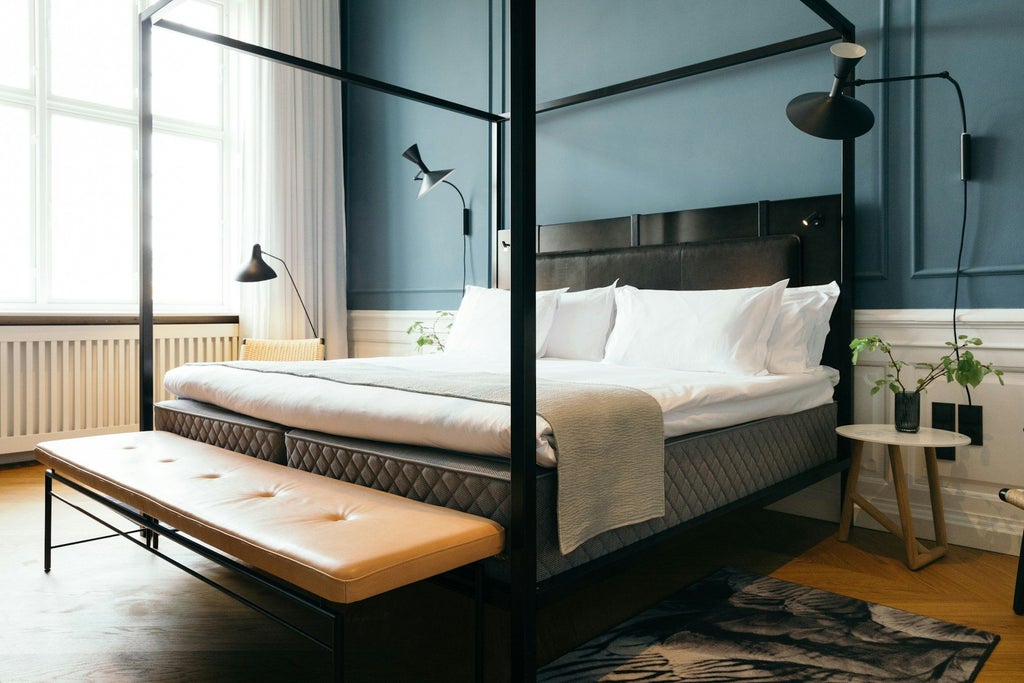 Elegantly designed Nobis Suite with contemporary Danish furnishings, plush king bed, modern artwork, and expansive city view in luxurious Copenhagen hotel room