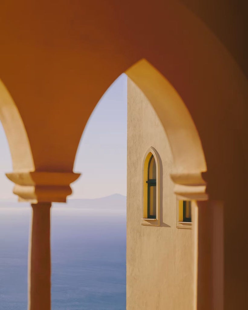 Historic stone archways frame an infinity pool overlooking the Amalfi Coast, with sweeping Mediterranean Sea views at sunset