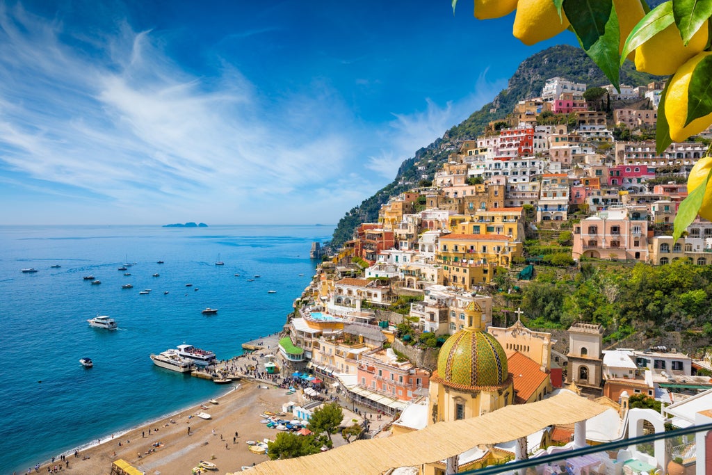 Mediterranean villas with vibrant bougainvillea cascade down steep cliffs overlooking turquoise waters of Italy's Amalfi Coast at sunset