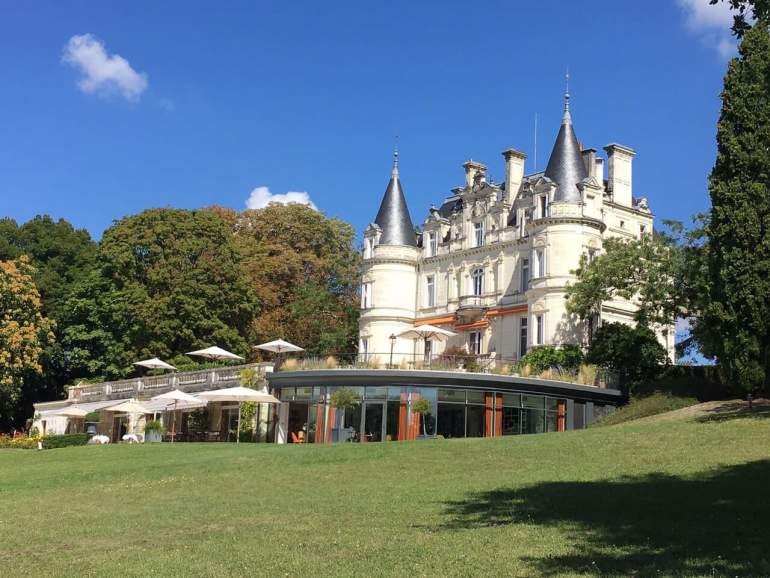 Elegant French château hotel with Renaissance architecture, surrounded by manicured gardens and reflecting in a serene pond at sunset